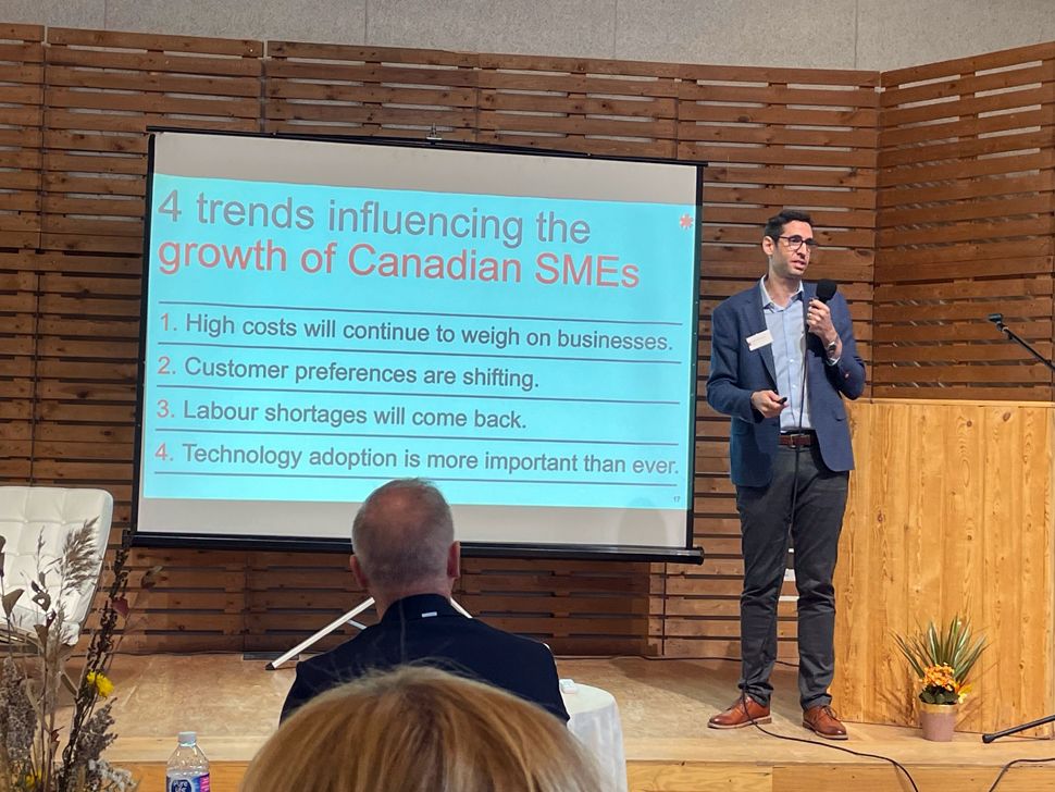 A man standing beside an overhead slide that lists four trends influencing the growth of Canadian SMEs.