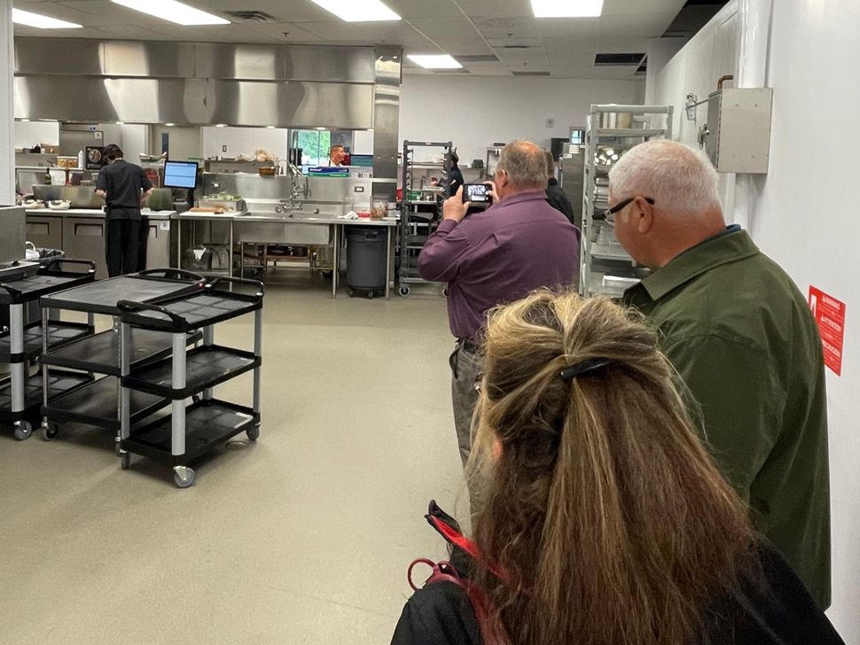 Three people looking into a commercial kitchen where two people are preparing food for a restaurant.