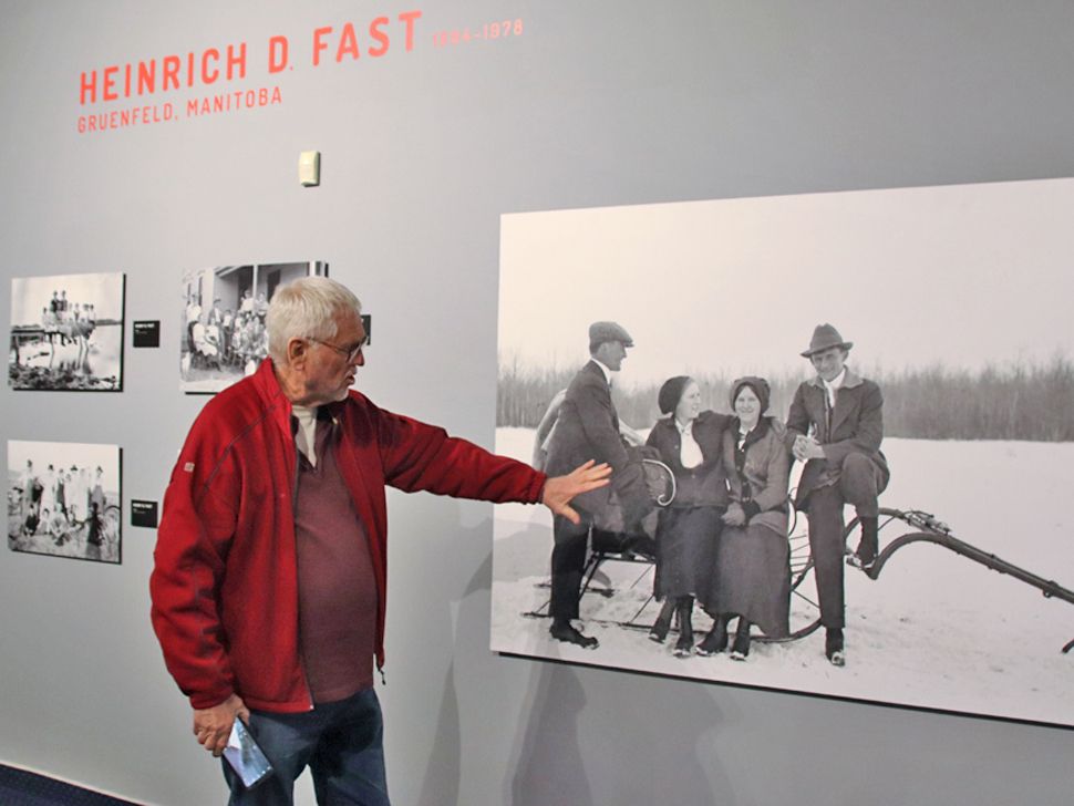 Local photographer, Dennis Fast stands beside photograph taken by his father, Heinrich D Fast. (2024)